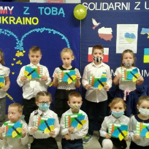 Uczniowie w ramach solidarności z walczącą Ukrainą prezentują laurki. W tle dekoracja w barwach Ukrainy. Kliknięcie na zdjęcie spowoduje jego powiększenie do rozmiaru oryginalnego.