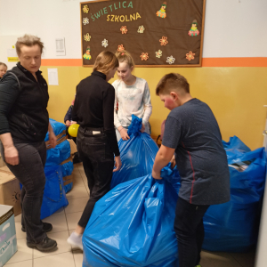 Uczniowie wraz z nauczycielką zawiązują worki z pomocą dla Ukrainy. Kliknięcie na zdjęcie spowoduje jego powiększenie do rozmiaru oryginalnego.