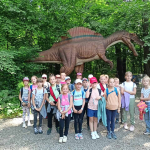 Uczniowie kl. II a w Parku Dinozaurów w Zatorlandzie. W tle stojąca makieta dinozaura. Kliknięcie na zdjęcie spowoduje powiększenie go do rozmiarów oryginalnych