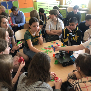 Uczniowie na spotkaniu dotyczącym sztucznej inteligencji oraz durku 3D. Na stole wydrukowane w czasie zajęć breloczki i inne elementy. Kliknięcie na zdjęcie spowoduje jego powiększenie do rozmiaru oryginalnego.