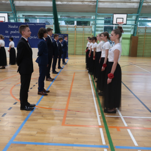 Walc w wykonaniu absolwentów.  Uczniowie stoją w szeregu ubrani w ciemne storoje galowe. Kliknięcie na zdjęcie spowoduje jego powiększenie do rozmiaru oryginalnego.