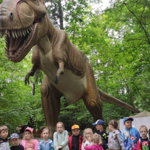 Przedszkolaki z Rudy Rysia w Parku Dinozatorland. Dzieci stoją w grupie. W tle makieta dinozaura. Kliknięcie na zdjęcie spowoduje jego powiększenie do rozmiaru oryginalnego.