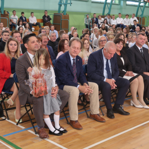 Zebrani goście  przedstawiciele władz RP, wojewódzkich oraz samorządowych zebrani na hali Zespołu Szkół w Szczurowej. Uczniowie Zespołu Szkół w Szczurowej grają na instrumentach. Dzieci ubrane w biało-czarne stroje. Uczniowie Zespołu Szkół w Szczurowej występują na akademii z okazji rozpoczęcia roku szkolnego 2023/2024. Dzieci ubrane w kolorowe stroje. W tle biało-niebieska dekoracja.Kliknięcie na zdjęcie spowoduje jego powiększenie do rozmiaru oryginalnego.