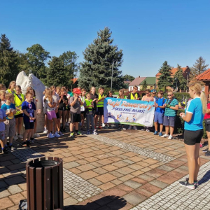 Uczestnicy rajdu "Pokolenie ma moc" zebrani na rynku w Szczurowej. Przed nimi pani Katarzyna Biedrońska. Wszyscy ubrani w sportowe ubrania, kaski i kamizelki odblaskowe. Kliknięcie na zdjęcie spowoduje jego powiększenie do rozmiaru oryginalnego.