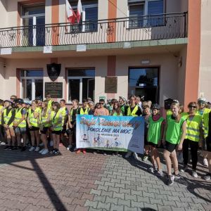 Uczestnicy rajdu "Pokolenie ma moc" stoją przed frontem budynku szkoły w Zaborowie. Ubrani są w odblaskowe kamizelki i sportowe ubrania, kaski. Trzymają baner przed sobą. Kliknięcie na zdjęcie spowoduje jego powiększenie do rozmiaru oryginalnego.