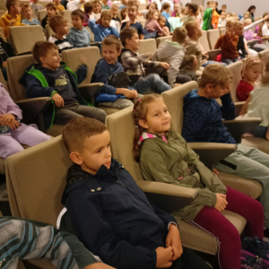 Uczniowie kl. 1-3 na przedstawieniu Kopciuszek w Brzesku. Dzieci siedzą na fotelach w brzeskiej bibliotece, ubrane są w kolorowe ubrania. Przed nimi kolorowa dekoracja baśni "Kopciuszek" Kliknięcie na zdjęcie spowoduje jego powiększenie do rozmiaru oryginalnego.