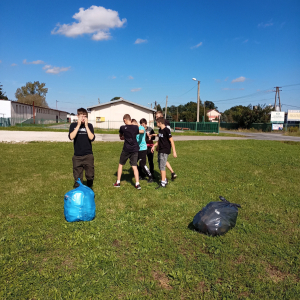 Uczniowie Szkoły Branżowej na Sprzątaniu Świata. Dzieci w sportowych ubraniach stoją przed studnią w Szczurowej. Trzymają w rękach worki. Kliknięcie na zdjęcie spowoduje jego powiększenie do rozmiaru oryginalnego.