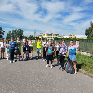 Uczniowie kl. V b na Sprzątaniu Świata. Dzieci w sportowych ubraniach stoją przed studnią w Szczurowej. Trzymają w rękach worki. Kliknięcie na zdjęcie spowoduje jego powiększenie do rozmiaru oryginalnego.