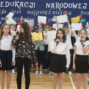 Występ uczennic kl. 6b. Dziewczynki śpiewają piosenki, w tle pozostałe dzieci i dekoracja. Kliknięcie na zdjęcie spowoduje jego powiększenie do rozmiaru oryginalnego.