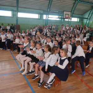 Uczniowie Zespołu Szkół w Szczurowej siedzą na akademii z okazji Dnia Nauczyciela. Dzieci ubrane w galowe stroje.  Kliknięcie na zdjęcie spowoduje jego powiększenie do rozmiaru oryginalnego.