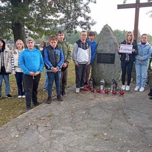 Uczniowie na Cmentarzu Parafialnym w Szczurowej stoją przed zbiorową mogiłą Romów. Dzieci ubrane w jesienne ubrania. Kliknięcie na zdjęcie spowoduje jego powiększenie do rozmiaru oryginalnego.