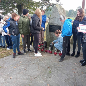 Uczniowie na Cmentarzu Parafialnym w Szczurowej stoją przed zbiorową mogiłą Romów, zapalają znicze. Dzieci ubrane w jesienne ubrania. Kliknięcie na zdjęcie spowoduje jego powiększenie do rozmiaru oryginalnego.