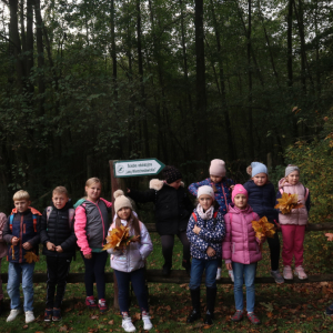 Uczniowie kl. 2 b stoją w grupie w lesie. Dzieci ubrane w kolorowe jesienne ubrania uczestniczą w wycieczce do Nadleśnictwa Dąbrowa Tarnowska. Kliknięcie na zdjęcie spowoduje jego powiększenie do rozmiaru oryginalnego.