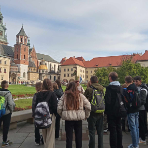 Uczniowie Zespołu Szkół w Szczurowej na wycieczce do Krakowa. Młodzież zgromadzona  przed Zamkiem Królewskim w Krakowie. Towarzyszy jej pani przewodnik i nauczyciele. Kliknięcie na zdjęcie spowoduje jego powiększenie do rozmiaru oryginalnego.