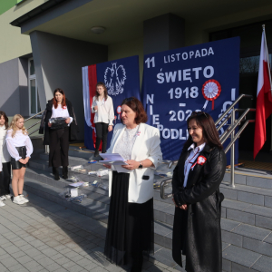 Pani Dyrektor Joanna Ozorka-Krawczyk wraz z panią Ewą Borowiec i uczestnikami konkursu Laurka dla Niepodległej. W tle dekoracja z symbolami narodowymi, flagą Polski i okolicznościowymi napisami. Uczestnicy ubrani w galowe stroje. Kliknięcie na zdjęcie spowoduje jego powiększenie do rozmiaru oryginalnego.