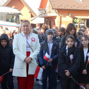 Dyrekcja, księża, nauczyciele i uczniowie Zespołu Szkół w Szczurowej stoją zgromadzeni przed głównym wejściem do szkoły. Uczestnicy wydarzenia ubrani są w ciepłe jesienne ubrania w rękach trzymają biało-czerwone flagi. Kliknięcie na zdjęcie spowoduje jego powiększenie do rozmiaru oryginalnego.