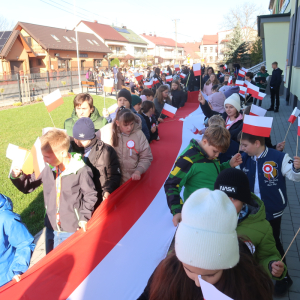 Uczniowie kl. 4a i b niosą długą biało-czerwoną flagę. Za nimi pozostali uczestnicy marszu. Kliknięcie na zdjęcie spowoduje jego powiększenie do rozmiaru oryginalnego.