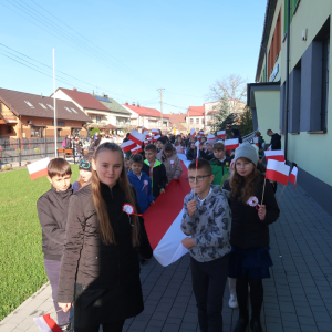 Uczniowie kl. 4a i b niosą długą biało-czerwoną flagę. Za nimi pozostali uczestnicy marszu. Kliknięcie na zdjęcie spowoduje jego powiększenie do rozmiaru oryginalnego.