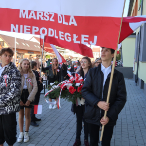 Uczniowie kl. 6b idą na czele uroczystego marszu z okazji Narodowego Święta Niepodległości. Chłopcy niosą biało-czerwony transparent z napisem "11 listopada Marsz dla Niepodległej" za nimi uczniowie kl. 4a,b niosą długą biało-czerwoną flagę oraz pozostali uczestnicy marszu. Kliknięcie na zdjęcie spowoduje jego powiększenie do rozmiaru oryginalnego.