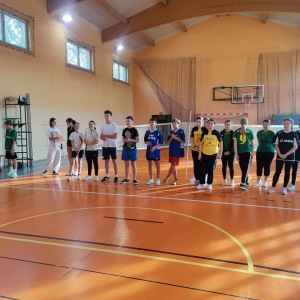 Uczestnicy zawodów w badmintonie stoją w szeregu na hali sportowej w Złotej. Zawodnicy i zawodniczki ubrani w kolorowe stroje sportowe. Kliknięcie na zdjęcie spowoduje jego powiększenie do rozmiaru oryginalnego.