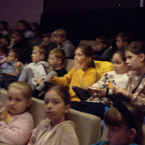 Uczniowie kl. 1-3 w Regionalnym Centrum Kulturalno-Bibliotecznym w Brzesku. Dzieci siedzą na sali na fotelach obok siebie. Słuchają i oglądają projekcję dotyczącą reklamy, a następnie film animowany. Na sali panuje ciemność. Kliknięcie na zdjęcie spowoduje jego powiększenie do rozmiaru oryginalnego.