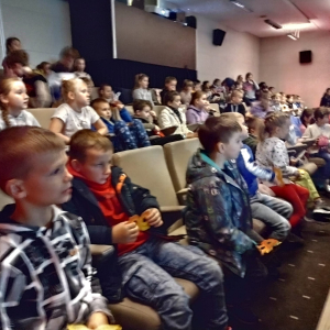 Uczniowie kl. 1-3 w Regionalnym Centrum Kulturalno-Bibliotecznym w Brzesku. Dzieci siedzą na sali na fotelach obok siebie. Słuchają i oglądają projekcję dotyczącą reklamy, a następnie film animowany. Na sali panuje ciemność. Kliknięcie na zdjęcie spowoduje jego powiększenie do rozmiaru oryginalnego.