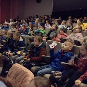 Uczniowie kl. 1-3 w Regionalnym Centrum Kulturalno-Bibliotecznym w Brzesku. Dzieci siedzą na sali na fotelach obok siebie. Słuchają i oglądają projekcję dotyczącą reklamy, a następnie film animowany. Na sali panuje ciemność. Kliknięcie na zdjęcie spowoduje jego powiększenie do rozmiaru oryginalnego.