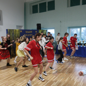 Uczestnicy Szkolnego Konkursu "Mam Talent" wspólnie tańczą na sali gimnastycznej. W tle tematyczna dekoracja. Kliknięcie na zdjęcie spowoduje jego powiększenie do rozmiaru oryginalnego. 