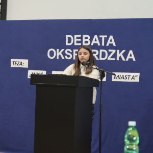 Uczestnicy biorący udział w Debacie Oksfordzkiej stoją przy mównicy. W tle tematyczna dekoracja. Kliknięcie na zdjęcie spowoduje jego powiększenie do rozmiaru oryginalnego.