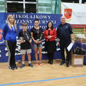 Rodzice z uczniami z medalami i nagrodami wręczonymi na  Mikołajkowym Rodzinnym Turnieju Badmintona. W tle tematyczna dekoracja. Kliknięcie na zdjęcie spowoduje jego powiększenie do rozmiaru oryginalnego.