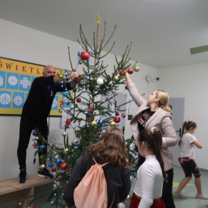  Uczniowie kl. 4 wraz z nauczycielami ubierają żywe szkolne choinki. Pomagają im nauczyciel wychowania fizycznego oraz języka polskiego. Dzieci ozdabiają je kolorowymi bombkami, śnieżynkami, soplami oraz innymi ozdobami. Kliknięcie na zdjęcie spowoduje jego powiększenie do rozmiaru oryginalnego.