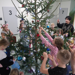 Uczniowie kl. 2 b wraz z wychowawcą dekorują choinkę. Zawieszają na jej gałązkach ozdoby. Kliknięcie na zdjęcie spowoduje jego powiększenie do rozmiaru oryginalnego.