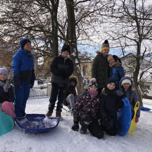 Dzieci stoją na wzniesieniu pokrytym śniegiem w parku. Trzymają w rękach jabłuszka, niektórzy siedzą na sankach. Kliknięcie na zdjęcie spowoduje jego powiększenie do rozmiaru oryginalnego.