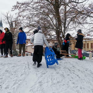 Wychowankowie wchodzą na ośnieżoną górkę. Trzymają w rękach sanki lub jabłuszka. Część dzieci stoi na ośnieżonym wzniesieniu w parku. Kliknięcie na zdjęcie spowoduje jego powiększenie do rozmiaru orygnianego.