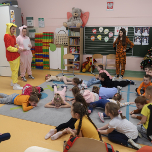 Przedszkolaki leżą na brzuchu na dywanie w swoje sali. Bawią się w zabawy przygotowane przez koleżanki ze starszych klas przebrane za postacie z Kubusia Puchatka. Kliknięcie na zdjęcie spowoduje jego powiększenie do rozmiaru oryginalnego.