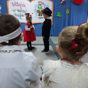 Dziewczynka przebrana za biedronkę mówi do mikrofonu wierszyk obok niej stoi chłopiec ubrany w czarny cylinder i elegancki strój. Kliknięcie na zdjęcie spowoduje jego powiększenie do rozmiaru oryginalnego.