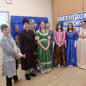 Uczniowie występujący w lekcji otwartej historii stoją przed dekoracją w grupie. Młodzież ubrana w długie suknie w różnych kolorach, chłopcy w stroje szlacheckie. Kliknięcie na zdjęcie spowoduje jego powiększenie do rozmiaru oryginalnego.