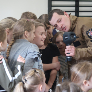 Dzieci wraz ze strażakiem testują działanie prezentowanego sprzętu. Kliknięcie na zdjęcie spowoduje jego powiększenie do rozmiaru oryginalnego.