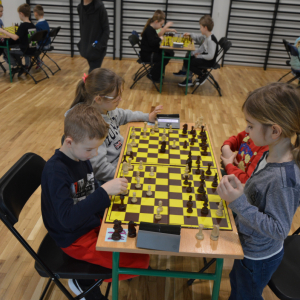 Dwoje dzieci siedzi przy stoliku. Grają w szachy na turnieju szachowym. Kliknięcie na zdjęcie spowoduje jego powiększenie do rozmiaru oryginalnego.