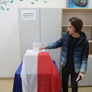 Uczeń kl. 7b wrzuca głos do urny wyborczej. Chłopiec stoi w bibliotece szkolnej.  Kliknięcie na zdjęcie spowoduje jego powiększenie do rozmiaru oryginalnego.