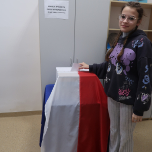 Uczennica kl. 8 stoi przy urnie wyborczej. Dziewczynka wrzuca oddany przez siebie głos.  Kliknięcie na zdjęcie spowoduje jego powiększenie do rozmiaru oryginalnego.