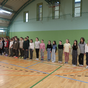 Młodzież stoi na baczność na hali gimnastycznej. Uczestniczą w akademii z okazji Dnia Żołnierzy Wyklętych. Towarzyszą im nauczyciele. Kliknięcie na zdjęcie spowoduje jego powiększenie do rozmiaru oryginalnego.