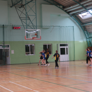 Dziewczęta biegają po hali gimnastycznej. Próbują przeciwniczką odebrać piłkę. Uczennice grają w koszykówkę. Kliknięcie na zdjęcie spowoduje jego powiększenie do rozmiaru oryginalnego.