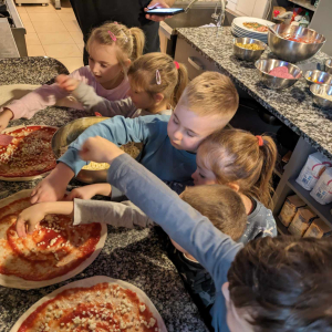 Grupka przedszkolaków układa na pizzach przygotowanych przez kucharza ulubione dodatki. Kliknięcie na zdjęcie spowoduje jego powiększenie do rozmiaru oryginalnego.