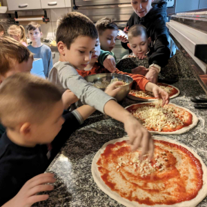 Chłopcy dekorują przygotowywane pizze mozzarellą oraz innymi składnikami. Pomaga im właścicielka pizzerii "Giona" pani Agnieszka Golik-Skura. Kliknięcie na zdjęcie spowoduje jego powiększenie do rozmiaru oryginalnego.