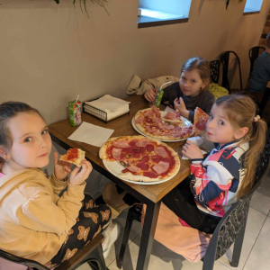 Trzy dziewczynki siedzą przy stole w pizzerii "Giona" . Trzymają w rękach kawałki pizzy, którą jedzą. Kliknięcie na zdjęcie spowoduje jego powiększenie do rozmiaru oryginalnego.