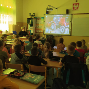 Uczniowie klas 1 oglądają na tablicy multimedialnej prezentację dotyczącą bezpieczeństwa na wsi. Dzieci siedzą w krzesełkach obok siebie. Kliknięcie na zdjęcie spowoduje jego powiększenie do rozmiaru oryginalnego.