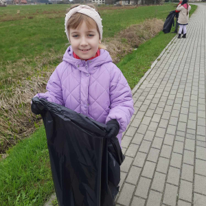 Milena Krysa z kl. 1 b trzyma worek ze śmieciami. Dziewczynka uczestniczy w akcji sprzątania swojej miejscowości. Kliknięcie na zdjęcie spowoduje jego powiększenie do rozmiaru oryginalnego.