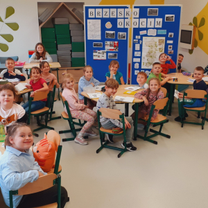 Dzieci siedzą w świetlicy szkolnej na krzesełkach przy stolikach. W tle stelaże z informacjami dotyczącymi Brzeska i Okocimia wykonanymi w ramach innowacji pedagogicznej. Kliknięcie na zdjęcie spowoduje jego powiększenie do rozmiaru oryginalnego.