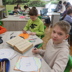 Chłopcy siedzą przy stolikach. Przygotowują papierowe pisanki z trudnościami ortograficznymi. Na środku słownik. Kliknięcie na zdjęcie spowoduje jego powiększenie do rozmiaru oryginalnego.